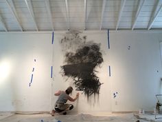 a man kneeling down in front of a black and white painting on the wall with blue tape