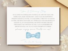 a white card with a blue bow tie on it next to flowers and an envelope