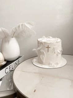 a white cake sitting on top of a table next to a vase filled with feathers