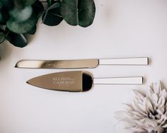 two knives sitting on top of a white table next to a potted plant and flower