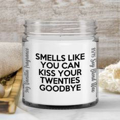 a candle that says smells like you can kiss your twenties goodbye next to a towel