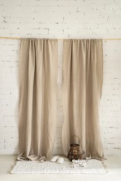 two beige curtains hanging on a brick wall with a white rug underneath them and a lantern in the corner