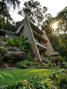 the house is surrounded by lush vegetation and large rocks, with sun shining on it