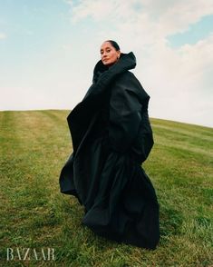 a woman in a black dress is sitting on the grass with her arms behind her head