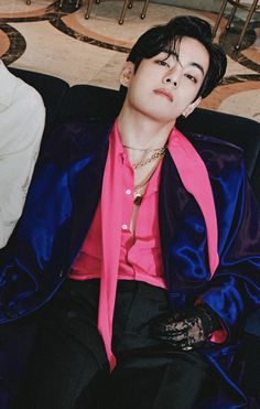 a young man wearing a pink shirt and black pants sitting on a blue velvet couch