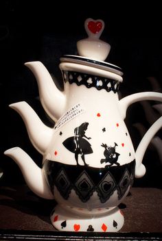 a white tea pot sitting on top of a table next to a black and white wall