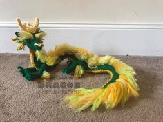 a green and yellow dragon figurine sitting on the floor next to a wall