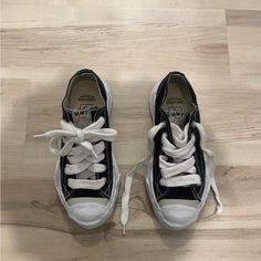 black and white tennis shoes with laces on the soles sitting on a wood floor