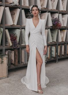 a woman standing in front of shelves wearing a white dress with long sleeves and high slit