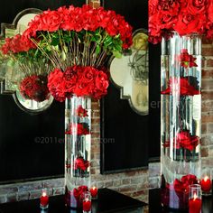 two tall vases filled with red flowers on top of a table next to each other