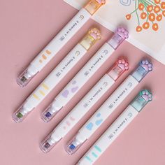 four pens are lined up next to each other on a pink surface with flowers and hearts