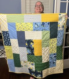 a woman is holding up a quilt made with squares and flowers in blue, green, yellow and white