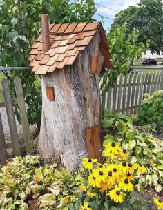 a tree stump with a house on it and some yellow flowers in the foreground