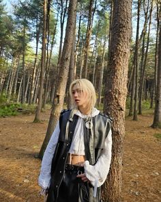 a woman standing next to a tree in the woods with her hand on her hip