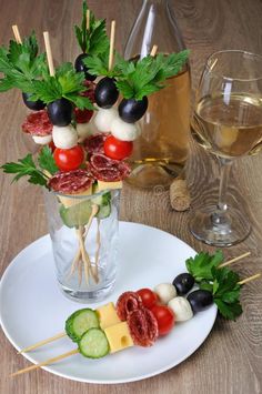 an appetizer with meat, cheese and vegetables on a plate next to a glass of wine