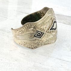 Vintage Silver Plated Southwestern Cuff Bracelet Beautifully Engraved Beautifully and meticulously engraved with enamel accents in navy blue at the center. The design is a mixture of geometric and flowing leaves or feathers pattern. The engraving is somewhat deep and likely not cast. Estimated to date from the 1970s. The cuff is 1 5/8 inches at the widest point. It measures 6 3/8 inches long plus the 7/8 inch opening. It can be adjusted but the metal gauge is heavy. Weighs 1.8 ounces. In good co Southwestern Engraved Cuff Bracelet As A Gift, Bohemian Adjustable Cuff Bracelet With Inlay, Western Style Stamped Cuff Bracelet, Southwestern Style Adjustable Etched Bracelets, Silver Bohemian Cuff Bracelet With Inlay, Bohemian Silver Cuff Bracelet With Inlay, Vintage Silver Hand Tooled Cuff Bracelet, Vintage Silver Hand-tooled Cuff Bracelet, Southwestern Style Adjustable Stamped Bangle