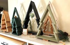 three wooden christmas trees sitting on top of a white counter next to a wall mounted clock