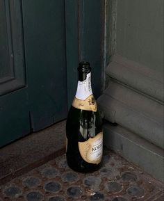 a bottle of wine sitting on the ground in front of a door with a green door