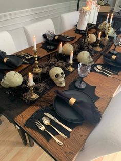 a table set with black and white plates, silverware, candles and skulls on it