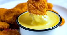 a person dipping something into a small white bowl filled with yellow sauce on top of chicken nuggets