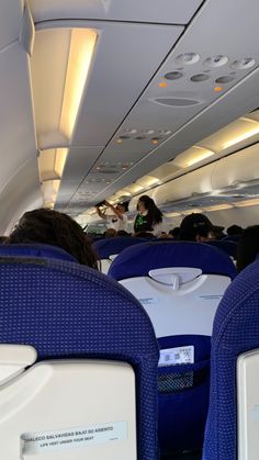 the inside of an airplane with people sitting on seats and one person standing in the aisle