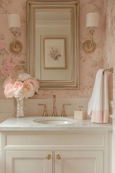 a bathroom with pink wallpaper and gold framed mirror above the sink, flowers in a vase on the counter