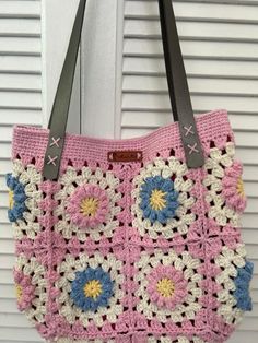 a pink crocheted bag hanging from a hook on a white door with shutters in the background