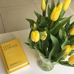 yellow tulips in a vase next to a book on a white countertop