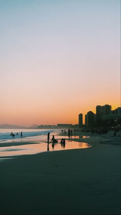 people on the beach at sunset with buildings in the backgrounnd and water