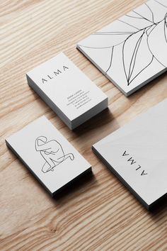 some business cards on a wooden table with white and black inked designs, including the logo