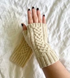 a woman's hand wearing knitted gloves on top of a bed