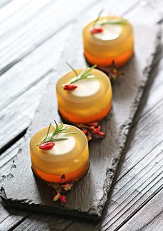 three small desserts are lined up on a slate board with rosemary garnishes