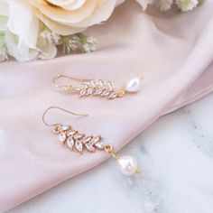 two pairs of earrings sitting on top of a pink cloth next to white and yellow flowers