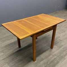 a wooden table sitting on top of a floor next to a gray wall in an empty room