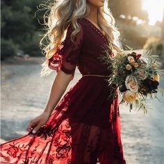 a woman in a red dress is walking down the street holding a bouquet and looking off into the distance