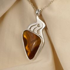 Designed to show off the dramatic bands of the agate, winding silver flows upward to the bail (loop). A very pretty champagne diamond can be traced back to just a hint of quartz crystals in the top of the agate. The agate has been set on a reflective background to show off its transparent, honey-colored stripes as if you were holding it up to a light. The overall effect makes the agate glow. It is set in a heavy bezel with a bright cut around its rim. The agate is 20 x 30 x 4.5 mm. Laguna Agate is a very highly prized for its colored banding. It is found in an area of Mexico that is south of El Paso, Texas. The 0.06 carat diamond is 2.5 mm. The pendant is 50 mm tall by 15 mm wide (about 2 x 1 inches). The sterling silver chain is included. Reflective Background, Laguna Agate, Jewelry Pictures, Silver Casting, Wifi Signal, Rubellite Tourmaline, Agate Pendant Necklace, Tourmaline Pendant, Jewelry Picture