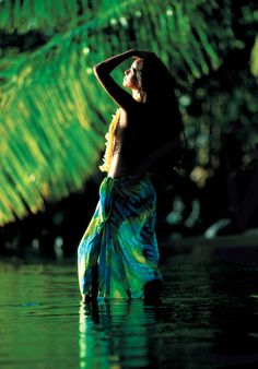 a woman is standing in the water with her arms behind her head and wearing a colorful dress