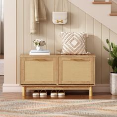 a wooden cabinet with shoes on it next to a stair case and potted plant