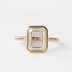 a gold ring with an emerald cut diamond in the center, on a white background