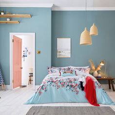 a bed room with a neatly made bed next to a blue wall and wooden shelves