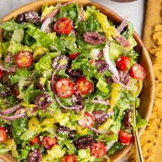 a salad with tomatoes, onions and olives in a wooden bowl on a table