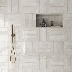 a bathroom with white tiles and a gold shower head in the corner next to it