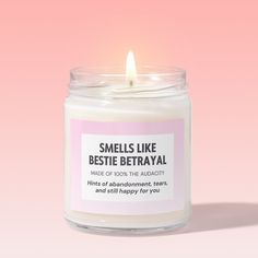 a white candle with a pink label on it that says smells like bestie betrayati made of 100 % the authority