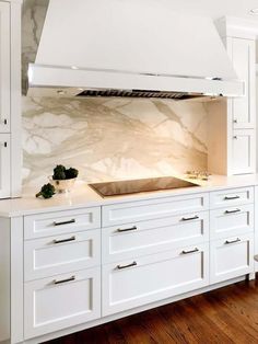 a kitchen with white cabinets and marble backsplash, an oven hood over the stove