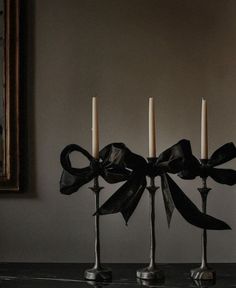 three candles with black bows on them sitting in front of a painting and a mirror