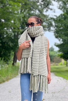 a woman is standing on the road wearing sunglasses and a scarf with fringes around her neck