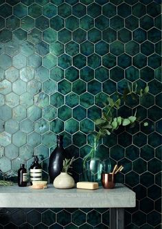 a shelf with vases and other items on top of it in front of a green tiled wall