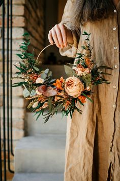 a woman holding a wreath with flowers and greenery on it in front of stairs