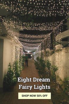 a man walking down a walkway covered in white lights and greenery on both sides