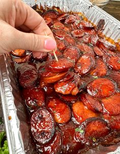 a person is holding a toothpick to some food in a tin foil pan